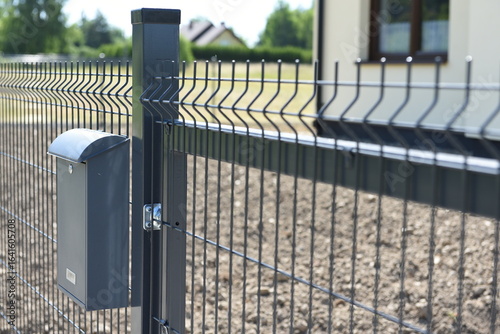 Detail of black steel mesh fence with mounted mailbox in front of new house.
