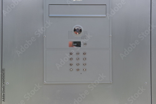 Close-up of modern intercom system with keypad, camera and speaker on metal surface.