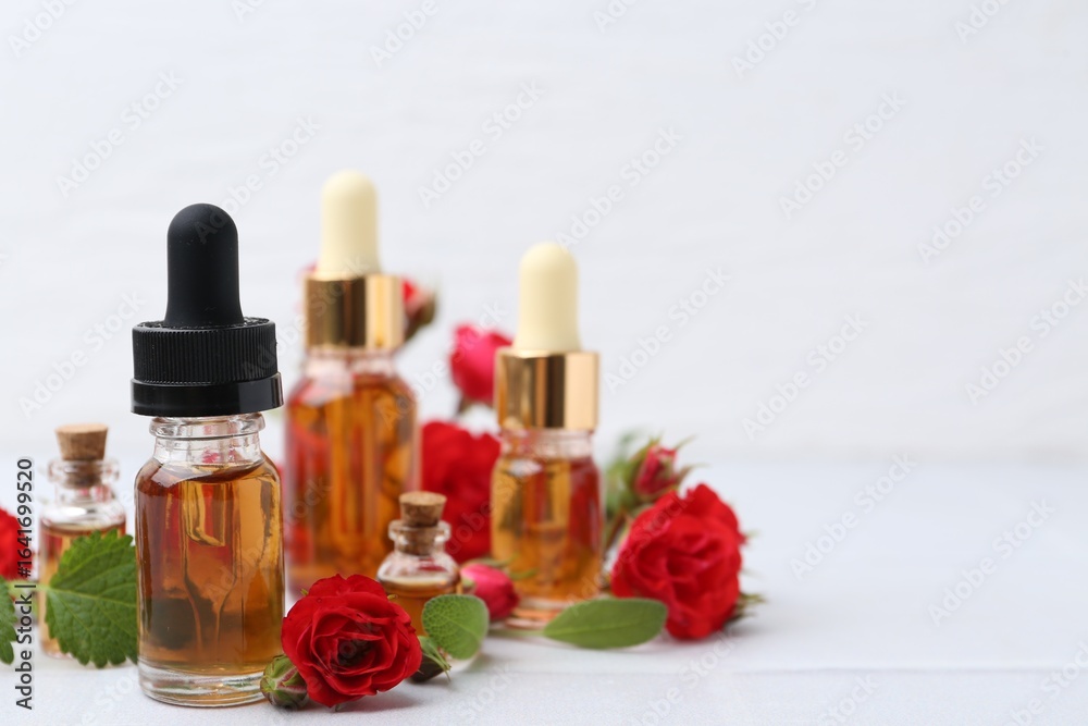Bottles of essential oil and red roses on white table, closeup. Space for text Bottles of essential oil and red roses on white table, closeup. Space for text