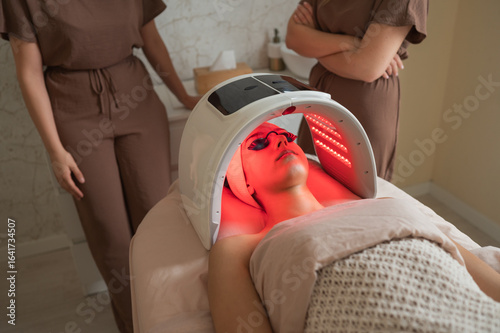 Bild auf Leinwand Estheticians overseeing red led light facial therapy in modern spa