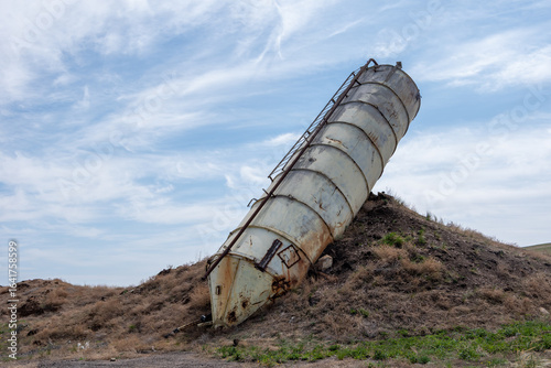 Tableau sur toile Rusty abandoned silo leaning on a grassy hill under a partly cloudy sky