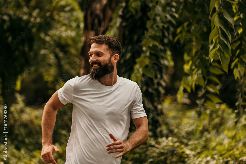 Obraz premium Happy bearded man running in green park enjoying exercise outdoors