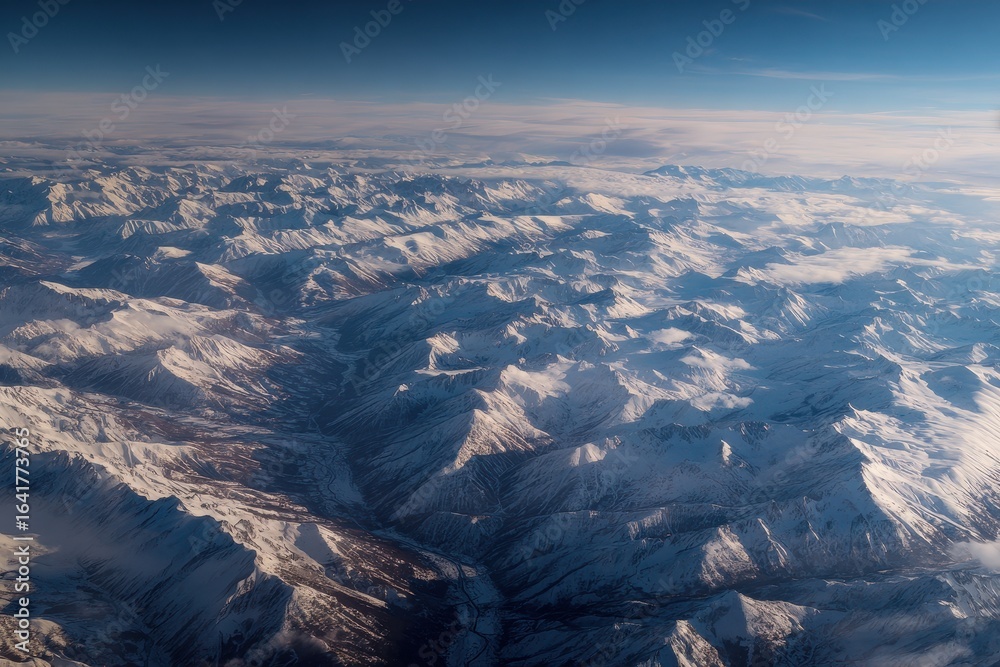 Obraz premium Snow-covered mountain range viewed from above during a clear daytime sky in winter