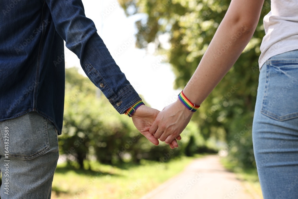 LGBT concept. Women in rainbow wristbands holding hands outdoors, closeup LGBT concept. Women in rainbow wristbands holding hands outdoors, closeup