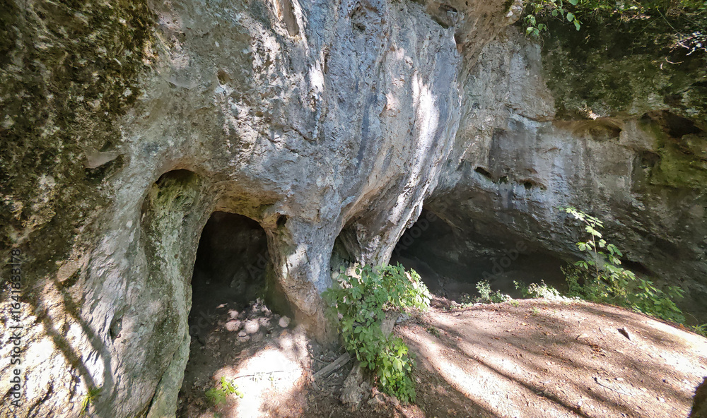 Obraz premium Closer perspective of a limestone cliff showing three cave openings side by side, with plants growing near the entrances, Bükk Mountains, Hungary.