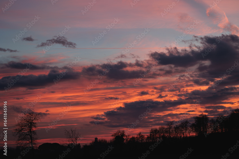 Obraz premium bellissimo e particolare tramonto dalle sfumature brillanti di colore arancione, visto da un ambiente naturale e rurale delle campagne del nord Italia, in inverno