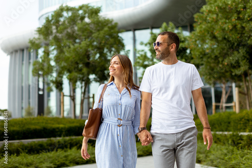 Obraz na plátně Couple enjoys a leisurely stroll hand in hand near modern architecture on a sunn