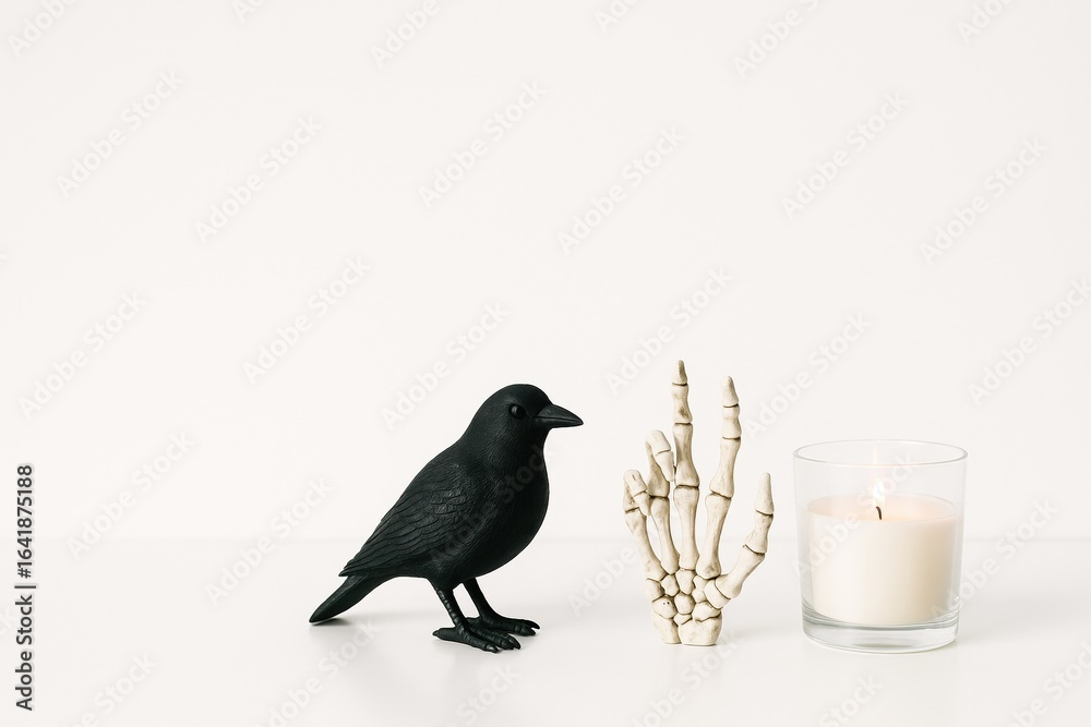 Obraz premium minimalistic halloween decor with black crow figurine, skeleton hand, and white candle on plain background