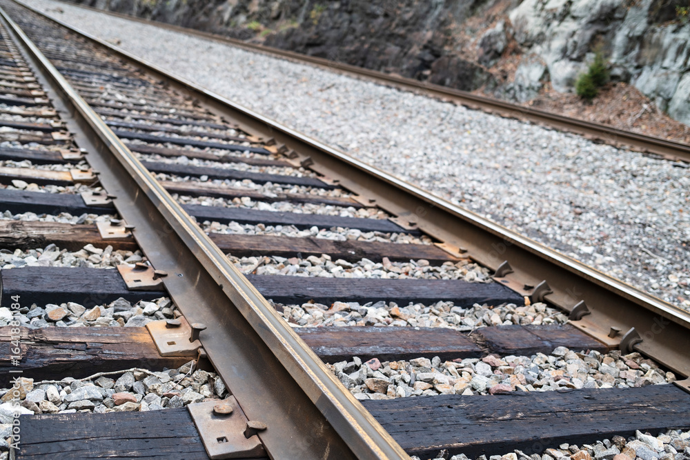 Naklejka premium A close-up view of railroad tracks, showcasing wooden ties, gravel ballast, and surrounding rocky terrain, capturing the essence of the railway infrastructure.
