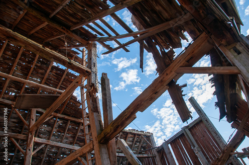 A unique perspective shot from inside a derelict barn, showing the dramatic collapse of the roof with a bright blue sky visible through the gaps.