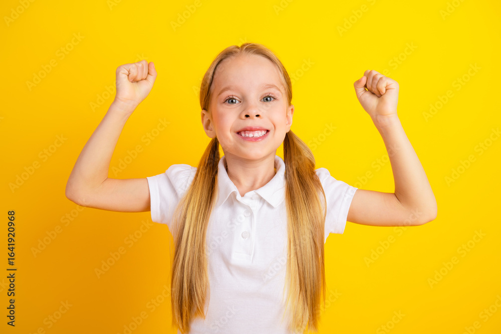 Pretty schoolgirl in white t-shirt celebrating with raised hands against vibrant yellow background Pretty schoolgirl in white t-shirt celebrating with raised hands against vibrant yellow background