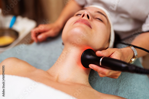 Tapeta Beautician performing radiofrequency lifting procedure on female patient's neck