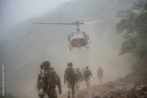 Fotografia Military helicopter hovers above uniformed soldiers walking on a muddy path in d