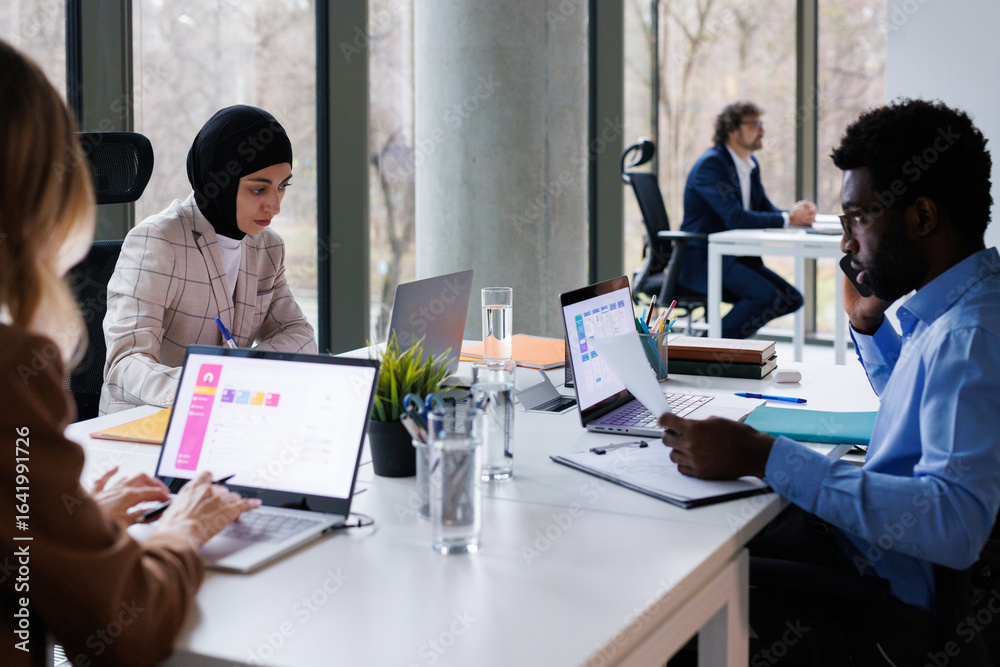 Multiracial co-workers concentrated on work sitting at table in office Multiracial co-workers concentrated on work sitting at table in office