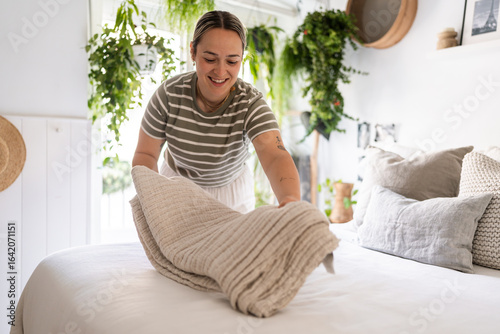 Housekeeper making bed in cozy bedroom with green plants