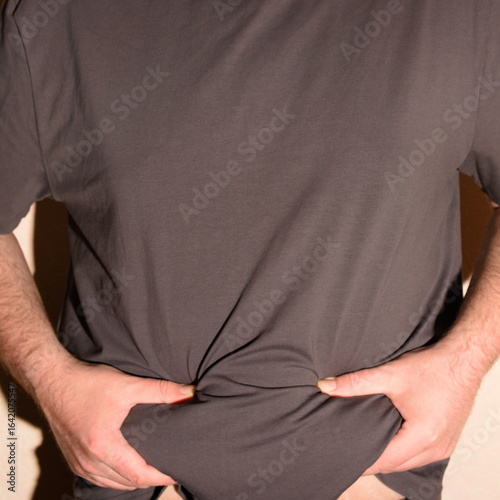 An obese man in a T-shirt shows his belly. Vertical shot
