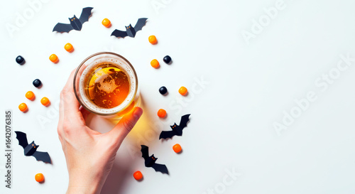 Halloween party with a hand holding a beer glass, bats, and candy on a white background, top view flat lay