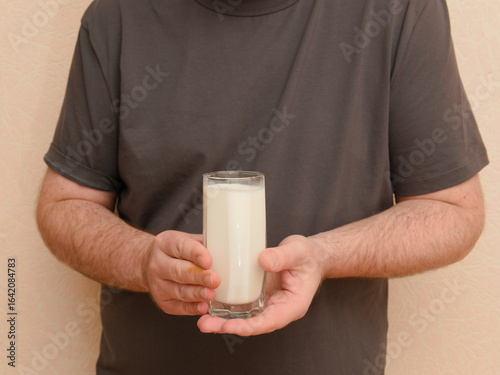 The man is holding a clear glass of milk.