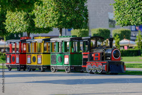 Colorful mini tourist train with red, yellow, and green carriages in a city park on a sunny summer day, outdoor attraction for children and families leisure transport for entertainment and sightseeing