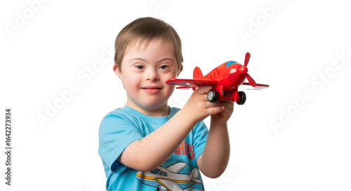 A smiling boy with down syndrome holding a red toy airplane in front of a black background smiling happy