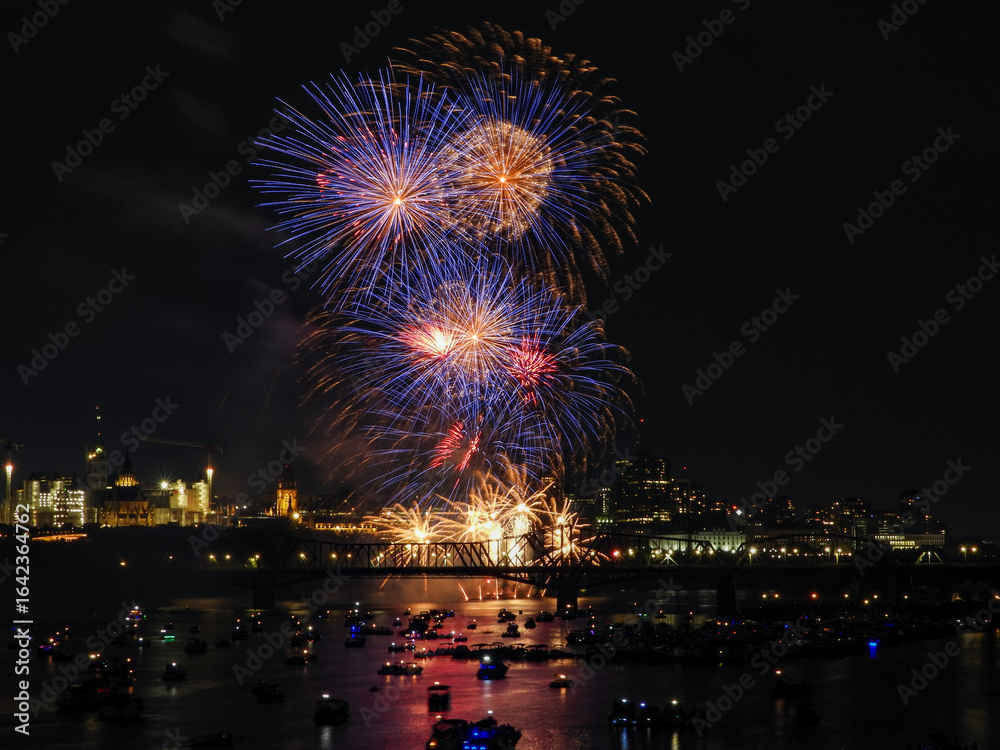 Fireworks in the night sky creating a bright display over the river filled with boating spectators Fireworks in the night sky creating a bright display over the river filled with boating spectators