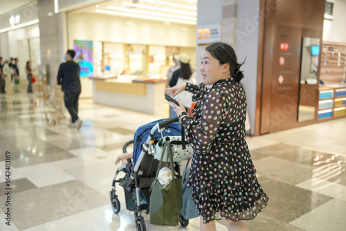 In a shopping mall parking lot, a Chinese family walks near their car while a one-year-old baby sits in a stroller, gently and safely pushed by a mother in her thirties. Spring. Shanghai. China.