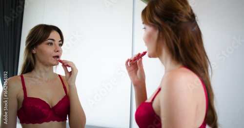 oung woman wearing a red lace lingerie set, standing in front of a mirror and applying lipstick.self-car and modern lifestyle oung woman wearing a red lace lingerie set, standing in front of a mirror 