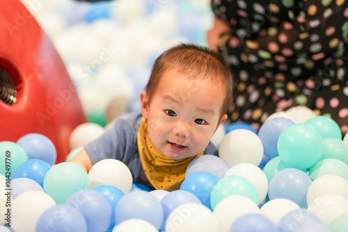 In an indoor play area, a one-year-old Chinese baby and her mother in her thirties play as if swimming in a pool of plastic balls. Hongkou District, Shanghai, China. Spring.