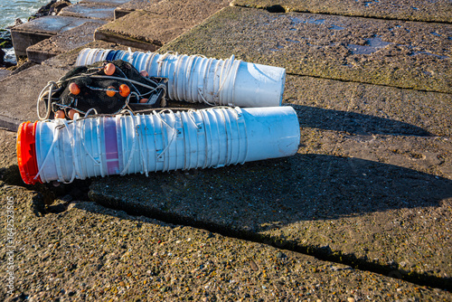 Two groups of empty paint buckets used to carry the fish caught with the net placed between them. The scene, captured on a concrete pier, highlights artisanal fishing practices and the practical reuse