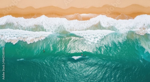 Aerial view of surfers riding waves in a vibrant ocean against a sandy beach backdrop