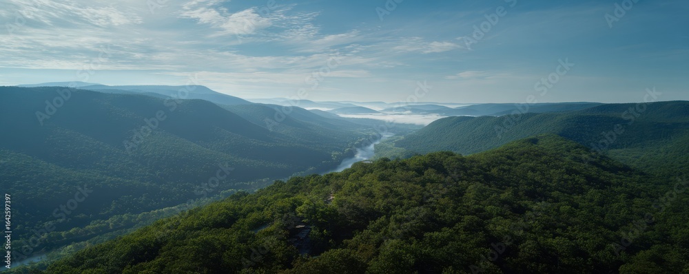 Fototapeta premium Verdant mountains roll toward the horizon under a partly cloudy blue sky, a river flows through