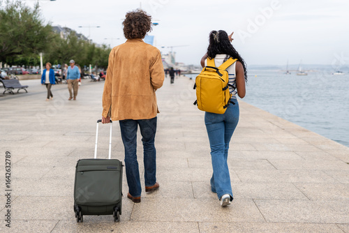 Tourists walking along the seaside promenade with luggage and backpack