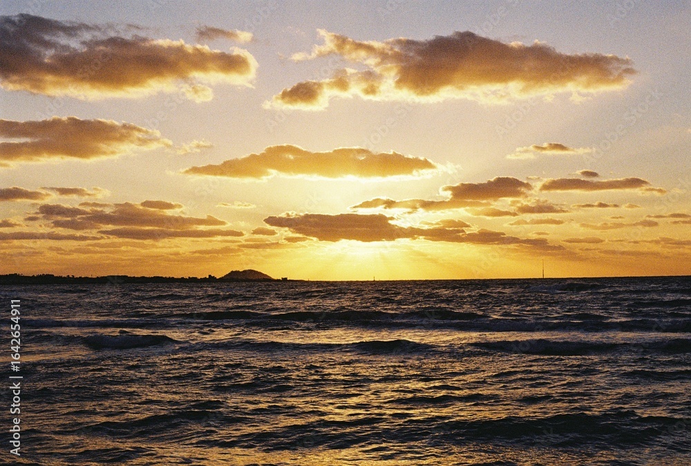 Obraz premium Golden sunset over the ocean with dramatic clouds and film grain texture