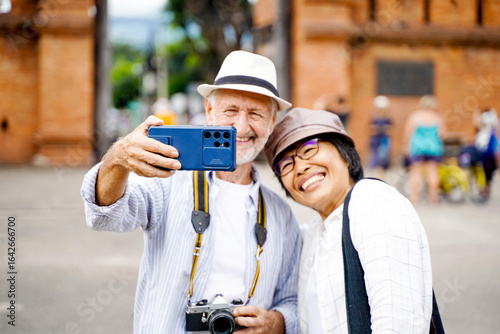 Closeup American senior tourist man with his wife take a photo selfie on blurred of city gate background. Senior tourist concept