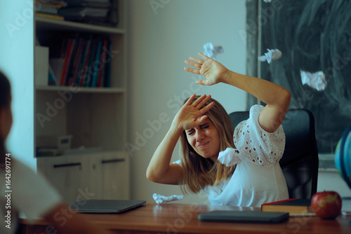Naughty Students Trowing Paper Balls at Stressed Teacher. Overwhelmed professor dealing with classroom bullying and aggressiveness towards herself 