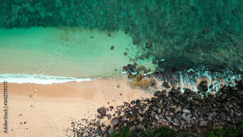 Aerial view of turquoise ocean waves meeting sandy beach and rocky shore.