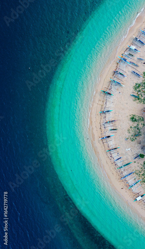 Drone shot of a sandy beach lined with traditional outrigger fishing boats.