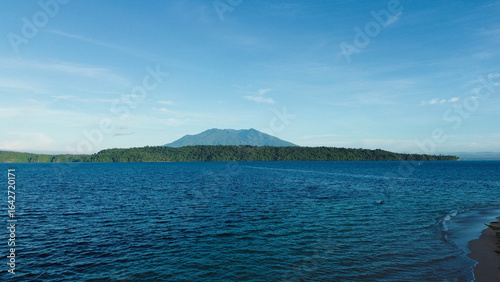 Aerial shot of serene island and dramatic volcanic mountain skyline.