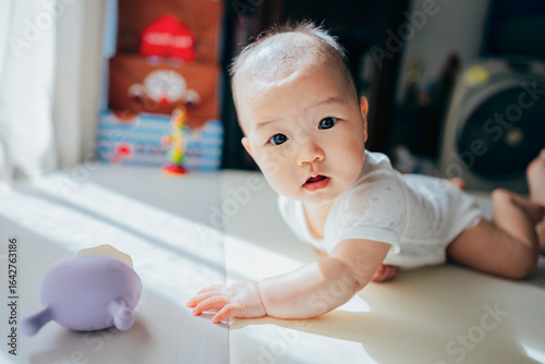A cute baby lies on the bed, smiling and looking directly at the camera with bright, curious eyes. Their joyful expression captures a moment of pure happiness and innocence.