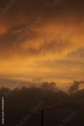 Industrial smokestack emitting dark smoke against a dramatic orange and gold sunset sky, symbolizing air pollution, environmental impact, and climate change awareness
