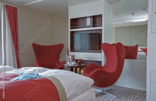 Luxurious suite stateroom cabin room onboard luxury yacht cruise ship cruiseship liner with bedroom and living area in red and creme with wood in modern Art Deco interior design