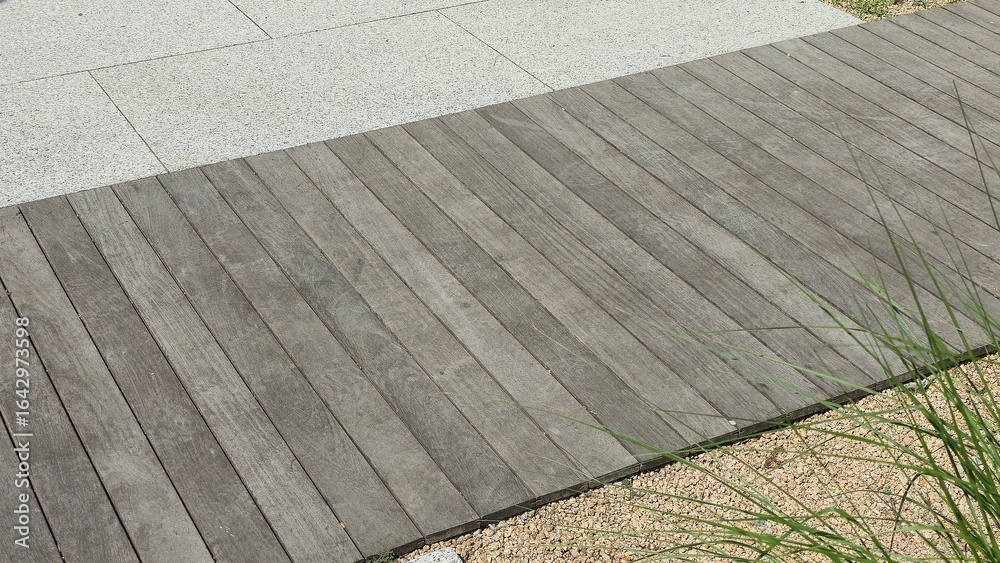 Fototapeta premium Wooden deck pathway combined with stone tiles and gravel creating a modern outdoor landscape design.