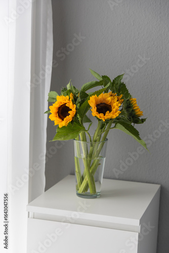 Sunflowers in a glass vase on a white table.