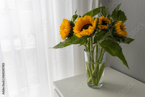 Sunflowers in a glass vase on a white table.