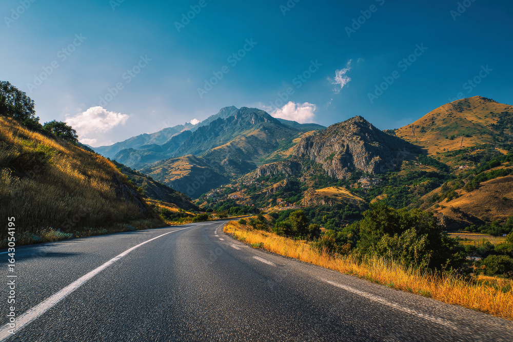 Fototapeta premium Breathtaking mountain road through lush green hills under a clear blue sky on a sunny day