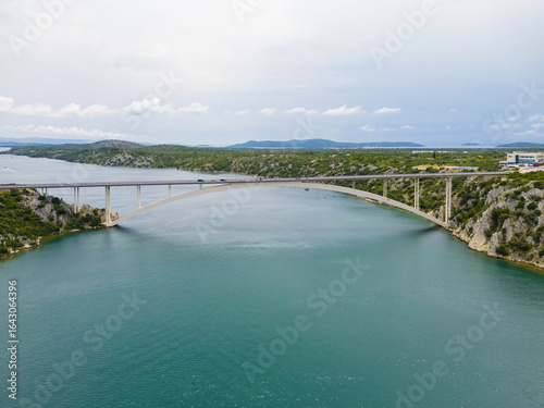 Wallpaper Mural Aerial view of a bridge arcing gracefully over the turquoise waters, connecting verdant shores under a vast, cloudy sky, Skradin, Sibensko-kninska Å¾upanija, Croatia. Torontodigital.ca