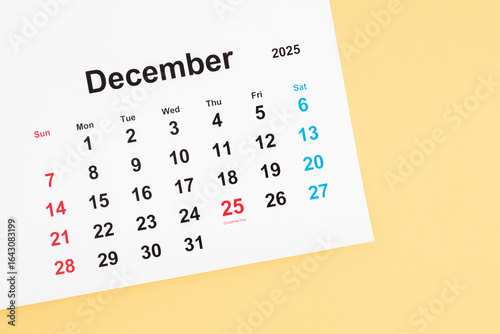 Top view of December 2025 calendar with date 25 marked, Christmas celebration on light yellow background