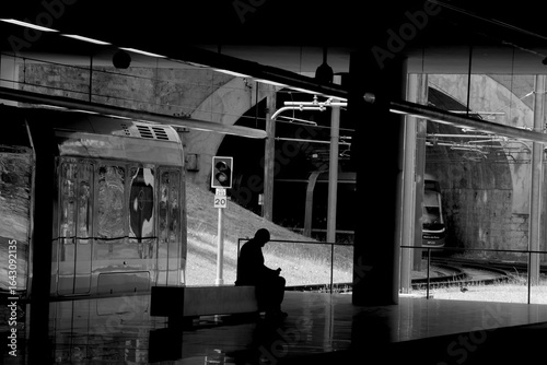 Black and white shot of lonely man sitting on the bench and waiting for train. Metro station Trindade. Porto, Portugal.