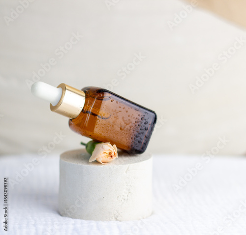 An elegant bottle in noble dark glass with natural serum and the most delicate cream to brighten your skin is decorated with an elegant flower on a plaster catwalk.