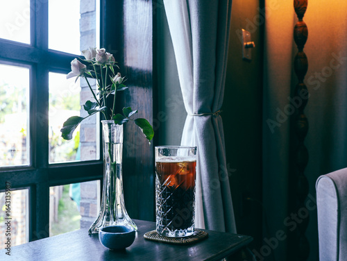 Glass of iced coffee with rose flower on table in coffee shop